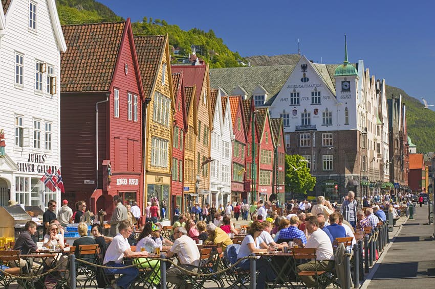 La gente se sienta en mesas frente a los coloridos edificios del distrito portuario de Bryggen en Bergen
