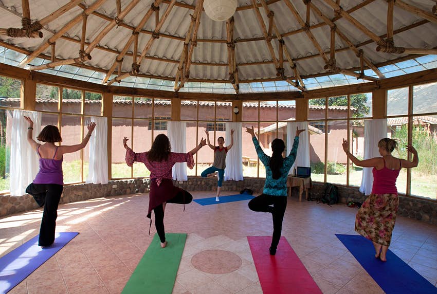 Cuatro mujeres toman una clase de yoga dirigida por un instructor en el estudio de yoga con paredes de vidrio en Nidra Vassi, Perú