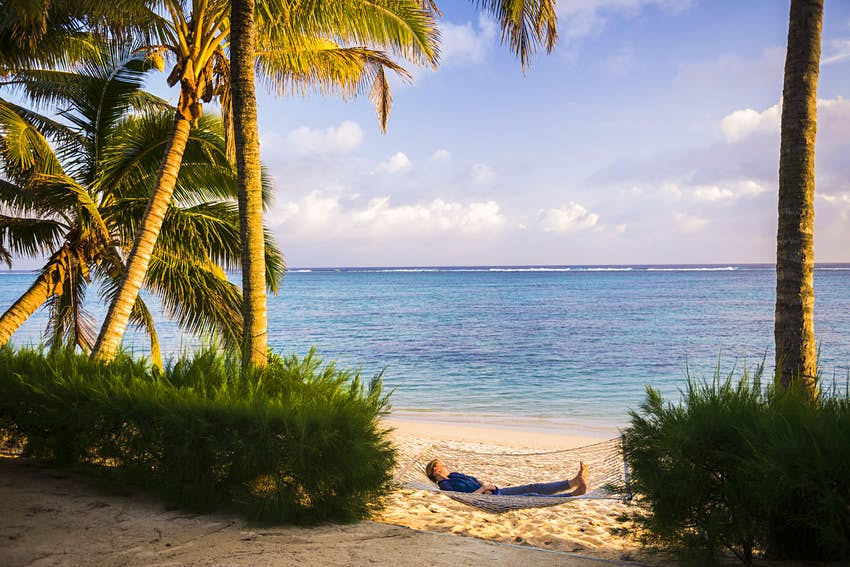 Mujer relajándose en una hamaca bajo palmeras en una playa tropical de arena blanca en Rarotonga