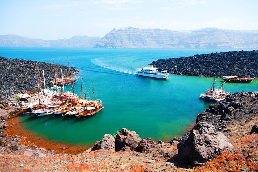 Una bahía en una isla volcánica con varios barcos llegando al pequeño puerto