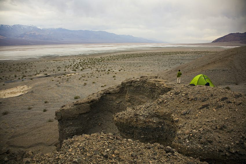Un hombre se para cerca de su tienda verde con vista al Parque Nacional Death Valley en California.