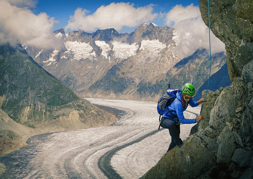 Un escalador trabaja en una roca cerca del glaciar Alech.  Detrás de él, se ve claramente un glaciar, como un glaciar blanco entre las montañas.