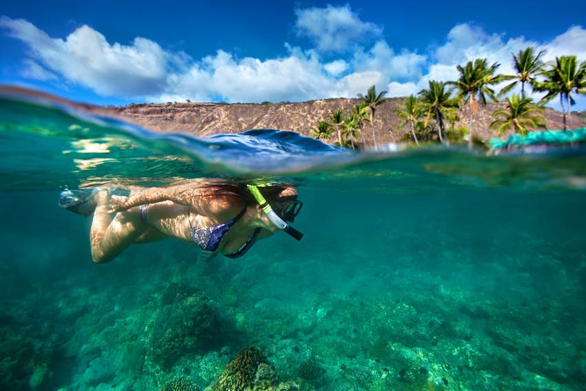 Una mujer bucea en una bahía de coral transparente, en una toma mitad dentro y mitad fuera del agua;  Experiencias de la Isla Grande