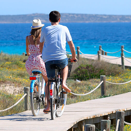Una pareja monta en bicicleta en la playa de Formentera