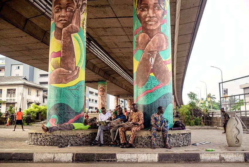 Los hombres están sentados y leyendo los periódicos de la mañana debajo del puente en Lagos.