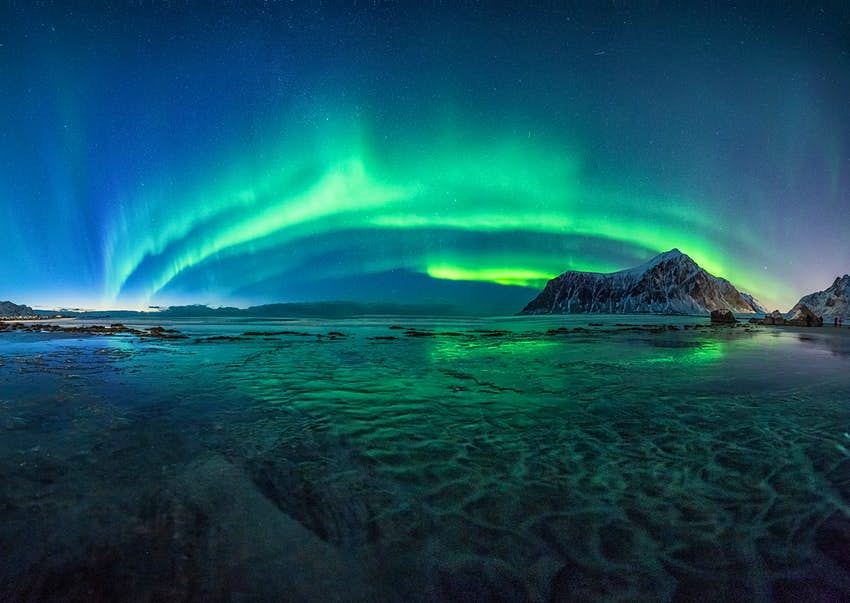 Las luces verdes de la aurora boreal iluminan el cielo nocturno de la playa de Skagsanden, Noruega.