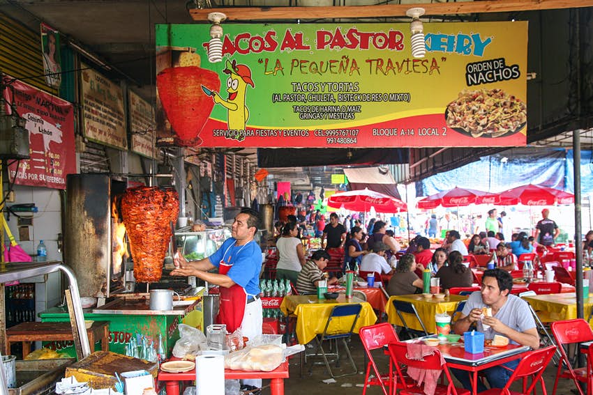 Un hombre corta carne para tacos al pastor entre mesas abarrotadas en el Mercado Municipal Lucas de Gálvez en Mérida.