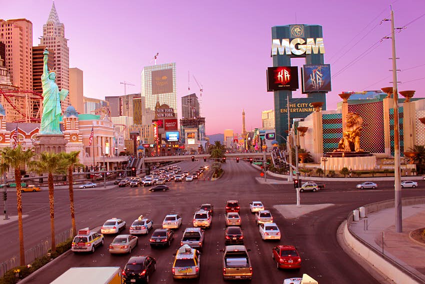 Los autos se alinean en un semáforo en el Strip de Las Vegas cerca de la intersección de MGM Grand y Casino con una puesta de sol rosa en el fondo
