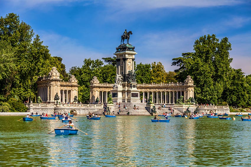 Monumento al Rey Alfonso XII, una enorme columnata con vistas al lago central en el Parque del Buen Retiro de Madrid con gente en botes de remos azules.