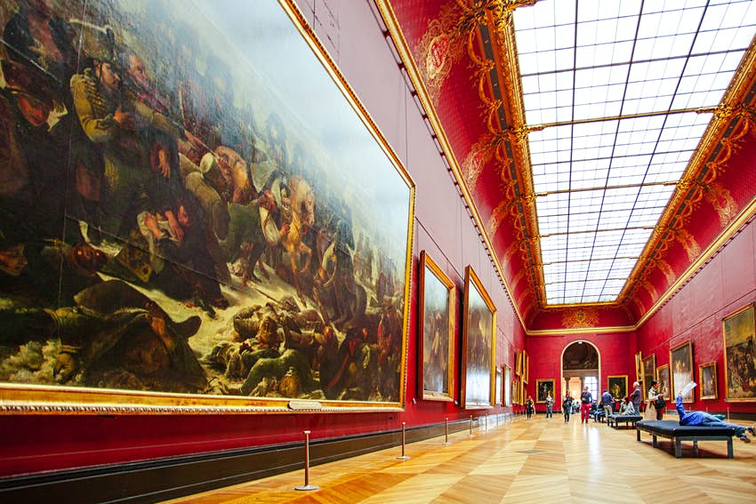 Los visitantes están en la galería roja del Museo del Louvre. 